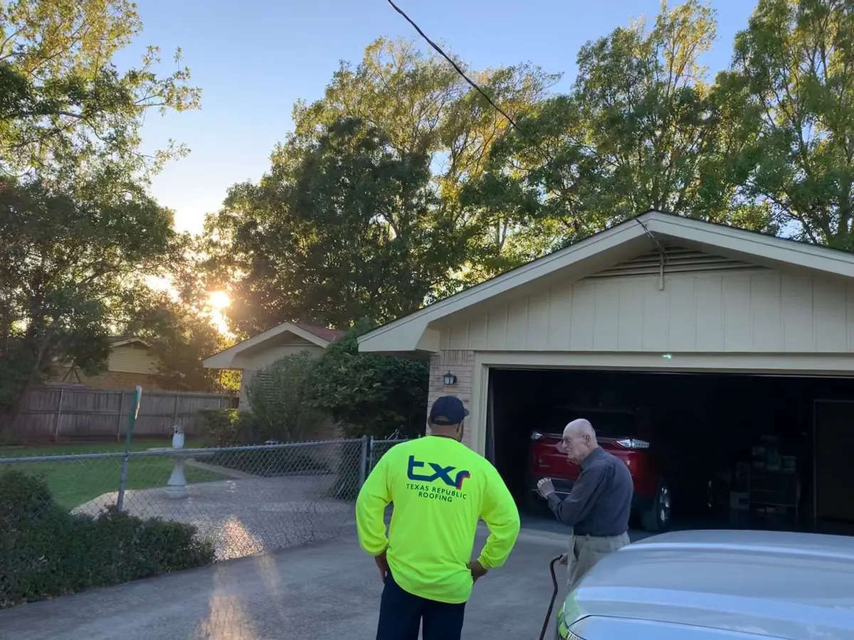 TXR roofer in a branded yellow shirt reviewing a roof with a homeowner outside an Arlington home